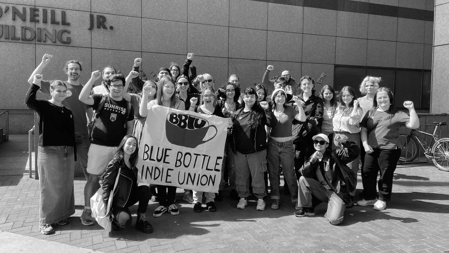 A group of people pose for a photo outside a government office, some with their fists in the air