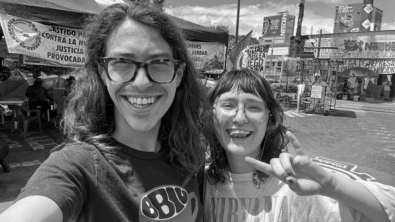 Selfie of two people with glasses and long hair smiling in front of a Nestlé factory in Colombia