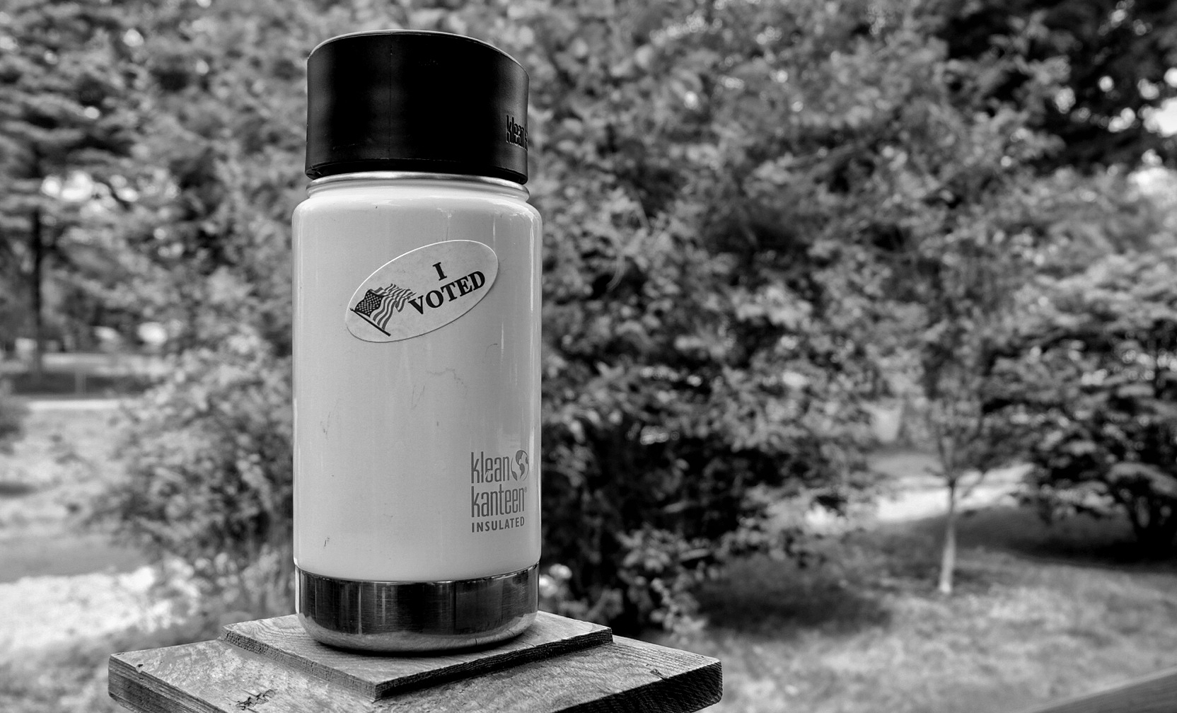 A reusable coffee cup on a fence post with an I Voted sticker