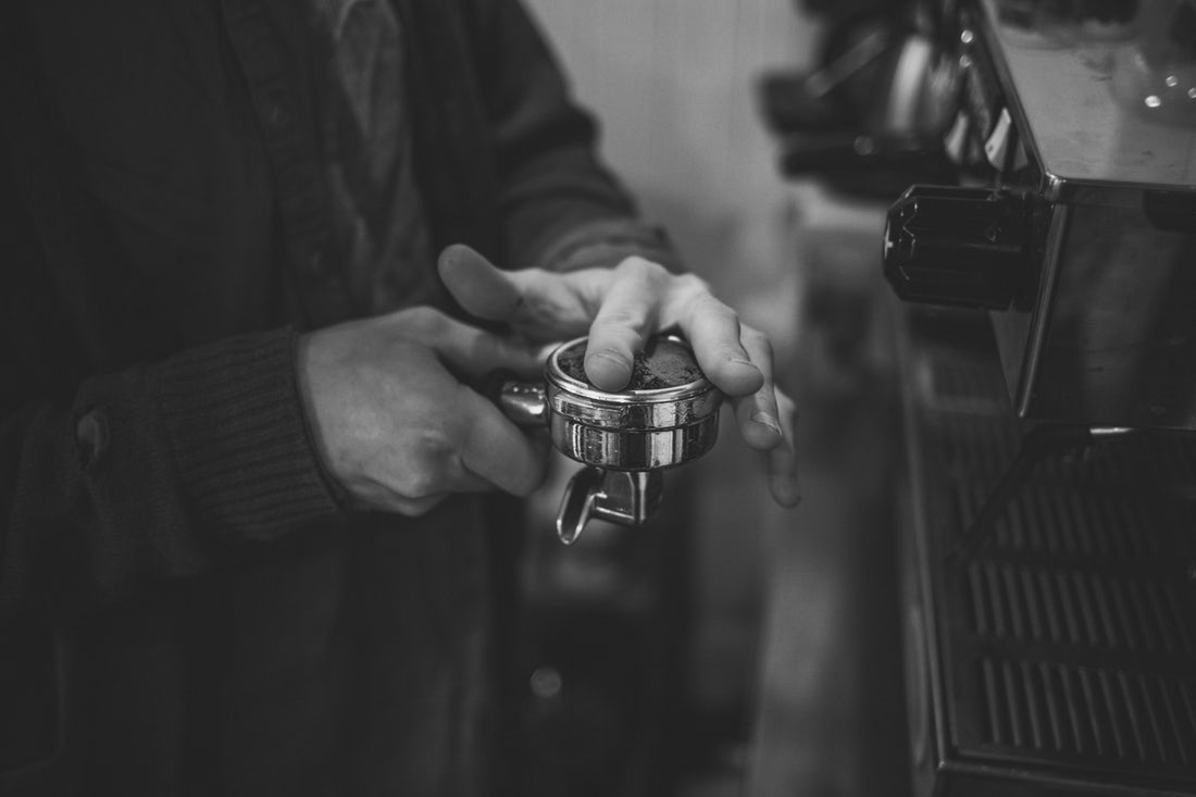 A barista smooths ground coffee in a portafilter with his finger.