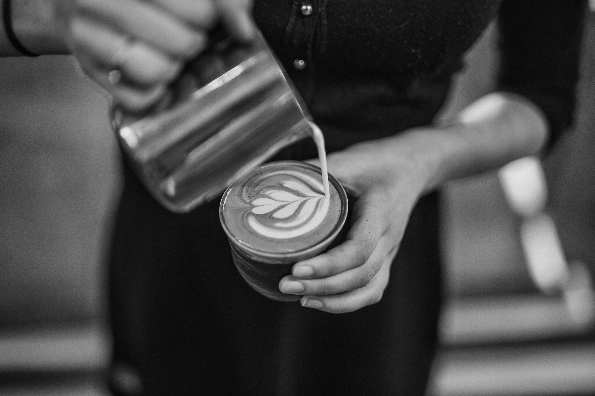 A barista pours latte art into a cup, seen from above