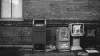A post box next to two newspaper dispensers surrounded by rubbish in front of a brick wall